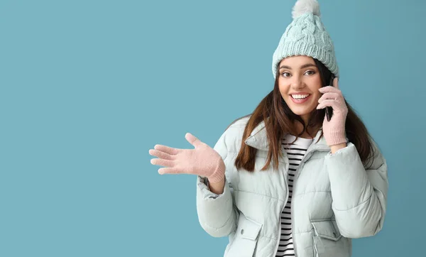 戴着温暖手套和帽子的年轻女子 用蓝色背景的手机交谈 — 图库照片