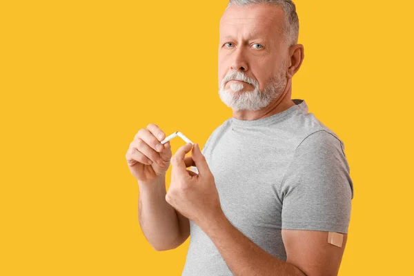 Mature man with applied nicotine patch and broken cigarette on color background. Smoking cessation