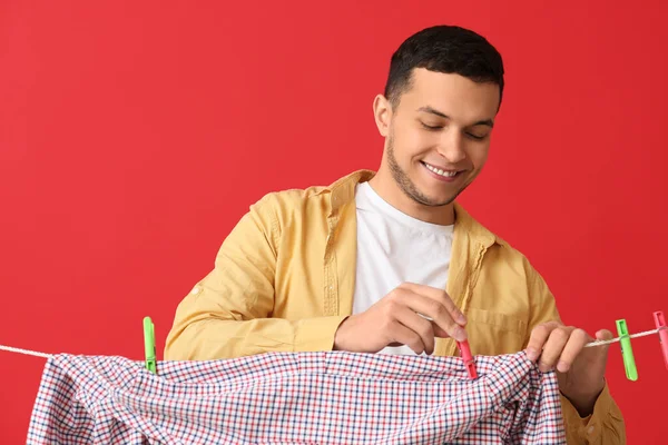 若いです男Hanglingクリーンシャツとともにプラスチック製の服ピンオン赤背景 — ストック写真