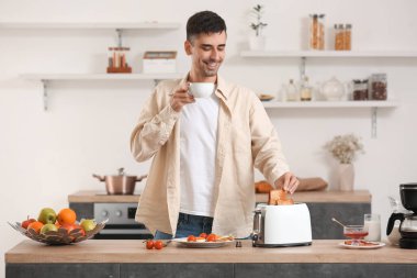 Genç adam kahve içiyor ve mutfakta lezzetli tost yapıyor.