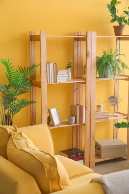 Oturma odasında sarı duvarın yanında dekoru olan ahşap kitaplık.