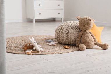Çocuk odasında puf ve oyuncak dolu hasır bir halı.