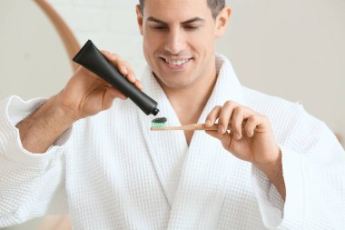 Yakışıklı genç adam banyoda aktif kömür diş macunu ile dişlerini fırçalıyor.