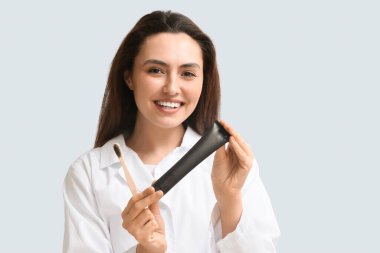 Aktif kömür diş macunu ve arka planda fırçası olan güzel bir genç kadın.