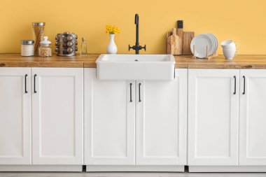 Lavabolu beyaz tezgahlar, mutfak aletleri ve sarı duvarın yanında yiyecek.