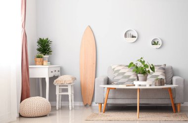 Tahta sörf tahtası, masası ve kanepesi olan aydınlık oturma odasının içinde.