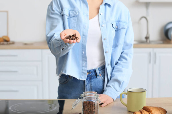 Young woman with coffee beans near counter in kitchen