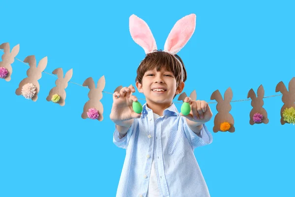 青い背景にウサギの耳とイースターエッグを持つ愛らしい男の子 — ストック写真