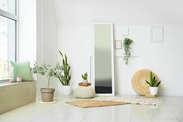 Interior of light living room with mirror, poufs and houseplants