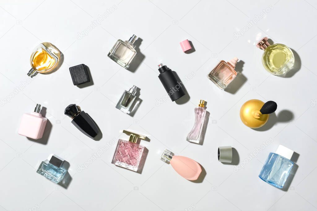 Bottles of different perfumes on light background, top view