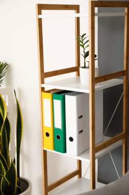 Gri ve beyaz duvarın yanında klasörleri olan raf ünitesi