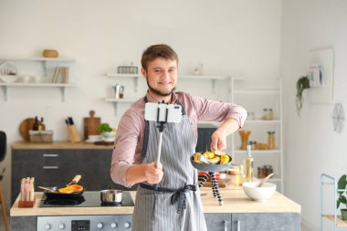 Kızarmış mısırlı genç adam mutfakta yemek pişirme videosu öğretiyor.