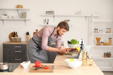 Genç adam mutfakta yemek yaparken not alıyor.