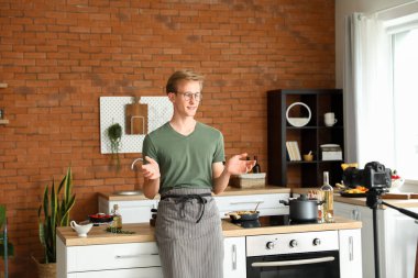 Yakışıklı genç adam mutfakta yemek pişirme videosu dersi kaydediyor.