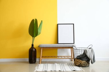 Çerçeveli modern bank, vazoda palmiye yaprakları ve renk duvarına yakın sepet.