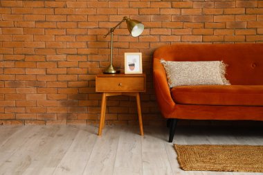 Altın lambalı masa, resim ve tuğla duvarın yanındaki kırmızı kanepe.