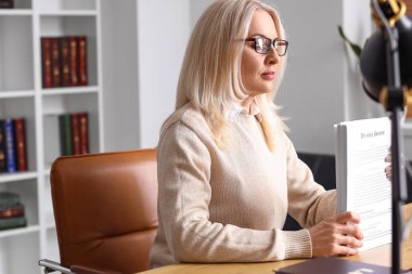 Elinde belgelerle mahkeme masasında oturan olgun bir kadın yargıç.