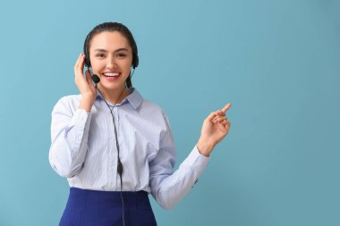 Mavi arka plandaki bir şeyi gösteren kulaklıklı genç ve güzel bir iş kadını.