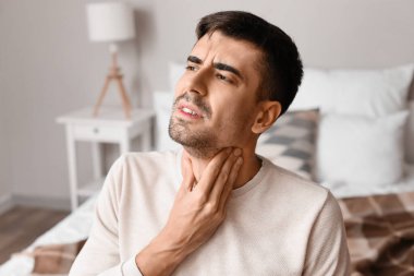 Evde boğazı ağrıyan genç bir adam.