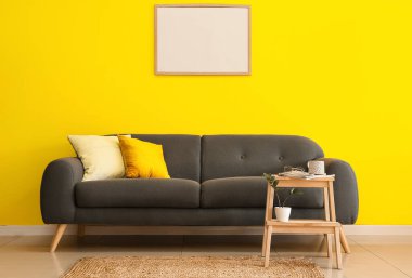 Şık bir kanepe ve sarı duvarın yanında ahşap bir tabure.