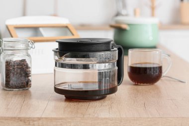 Mutfaktaki ahşap tezgahın üzerinde sıcak içecek ile kahve makinası, yakın plan.