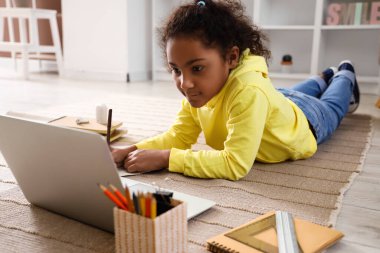 Küçük Afro-Amerikalı kız evde internet öğretmeniyle ders çalışırken deftere yazı yazıyor.