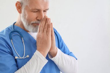 Olgun erkek doktor beyaz arka planda dua ediyor.