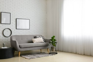 Kanepe, ev bitkisi ve beyaz tuğla duvarda boş fotoğraf çerçeveleri olan bir aydınlatma odası.