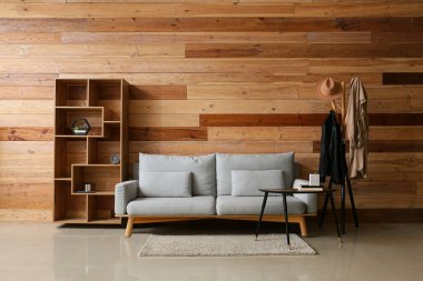 Odanın içinde kanepe, raf ünitesi ve ahşap duvarın yanında giysiler var.