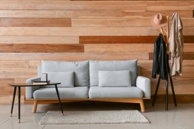 Masa kanepesi ve ahşap duvarın yanında giysileri olan bir oda.