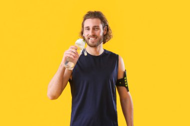 Turuncu arka planda bir şişe suyu olan sportif bir adam.