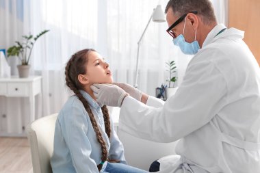 Doktor klinikte küçük kızın boynunu muayene ediyor.