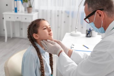 Doktor klinikte küçük kızın boynunu muayene ediyor.