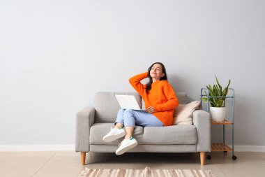 Evdeki kanepede dizüstü bilgisayarı olan güzel genç bir kadın.