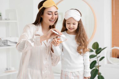 Anne küçük kızının banyodaki fırçasına diş macunu sürüyor.