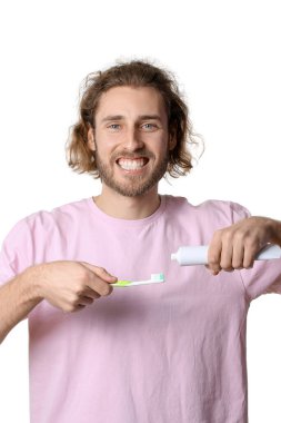Beyaz arka plandaki fırçaya diş macunu süren yakışıklı genç adam.