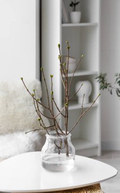 Işık odasındaki masanın üzerinde ağaç dalları olan vazo.