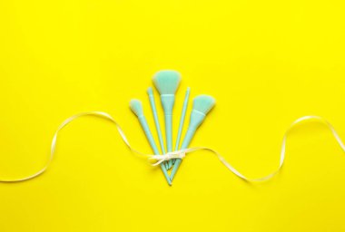 Makyaj fırçaları ve sarı arkaplanda kurdele ile kompozisyon