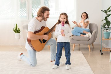 Babası evde gitar çalarken küçük kız mikrofona şarkı söylüyor.