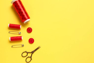 Sarı arkaplanda iplik makaraları, makas, düğmeler ve iğneler