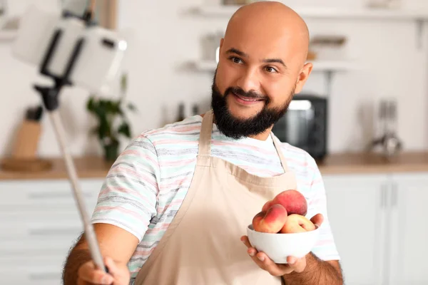 一个英俊的男人 带着一碗桃子 在厨房里记录视频教学 — 图库照片