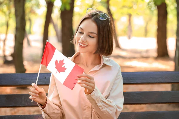 坐在户外长椅上的美丽的年轻女子 举着加拿大国旗 — 图库照片
