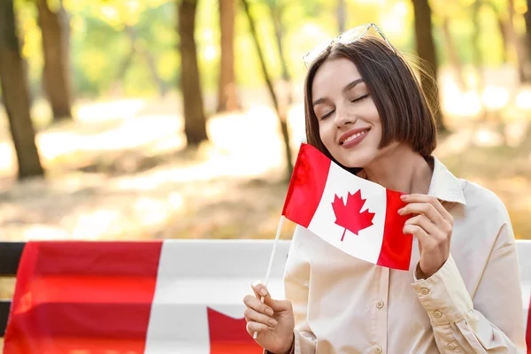 坐在户外长椅上的美丽的年轻女子 举着加拿大国旗 — 图库照片