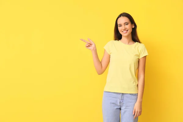 黄色の背景に何かを指すスタイリッシュなTシャツの美しい若い女性 — ストック写真
