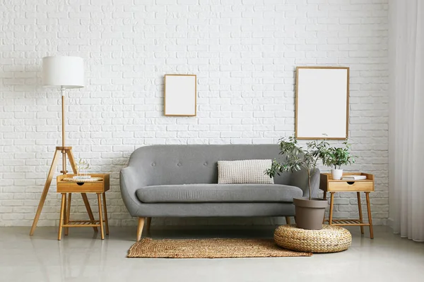 Comfortable sofa, houseplant and floor lamp near white brick wall in room interior