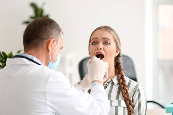 Doctor examining woman with sore throat in clinic