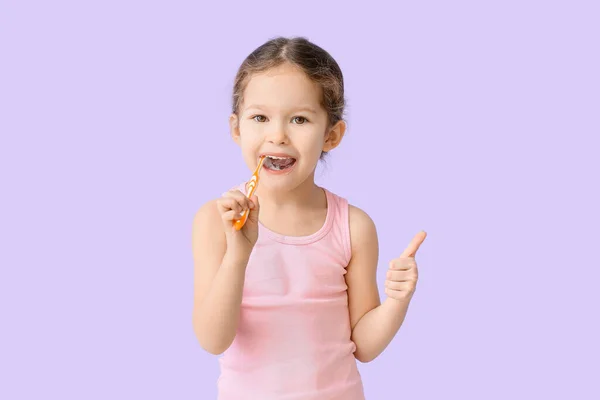 可爱的小女孩在淡紫色背景下刷牙 — 图库照片
