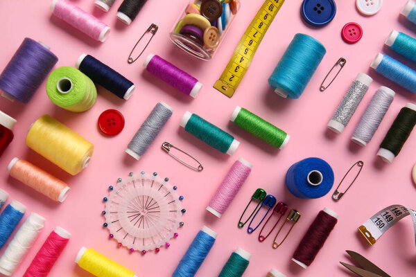 Thread spools, ball pins, measuring tape and buttons on pink background