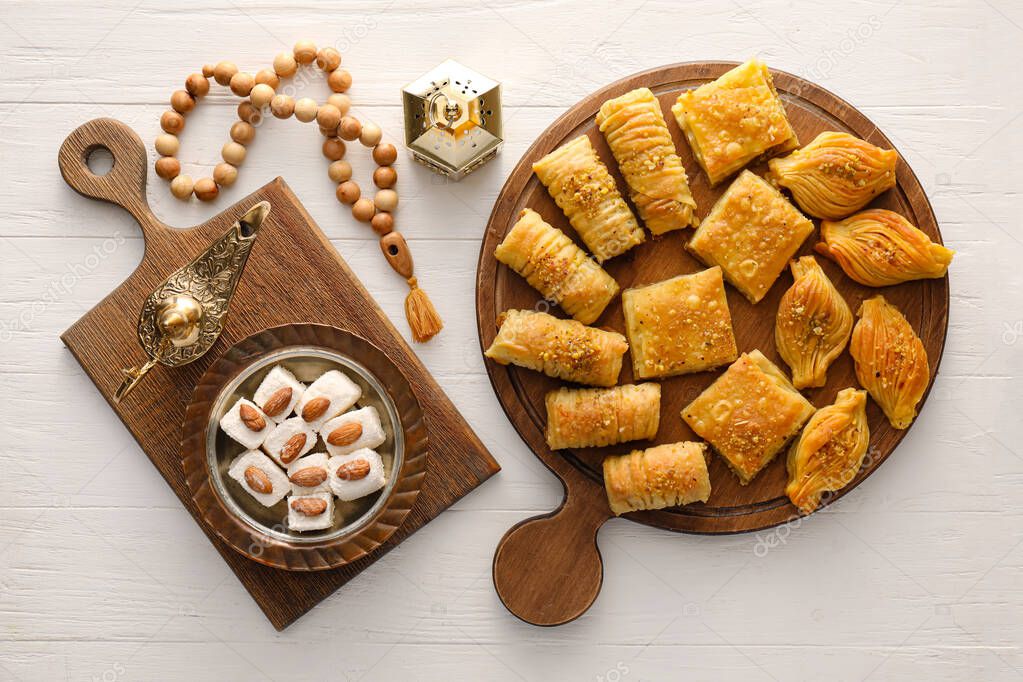 Tasty Eastern sweets with Arabic lamps and tasbih on white wooden background