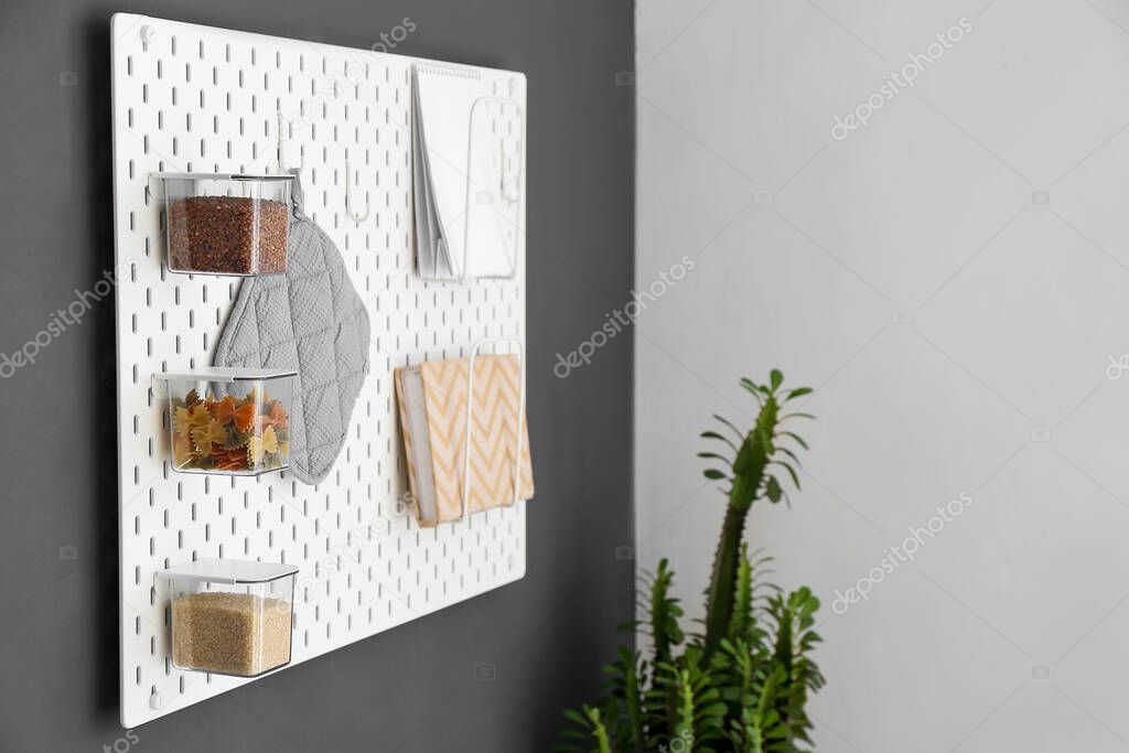 Pegboard with notebooks and jars with food on dark wall in kitchen